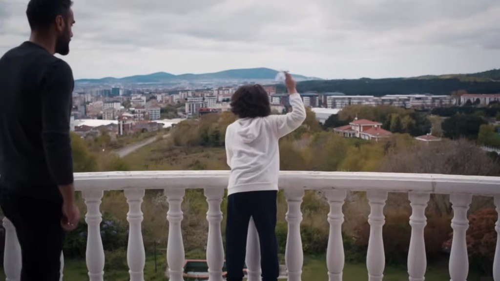 Yusuf wychyla się za balustradę tarasu, by wypuścić papierowy samolot.