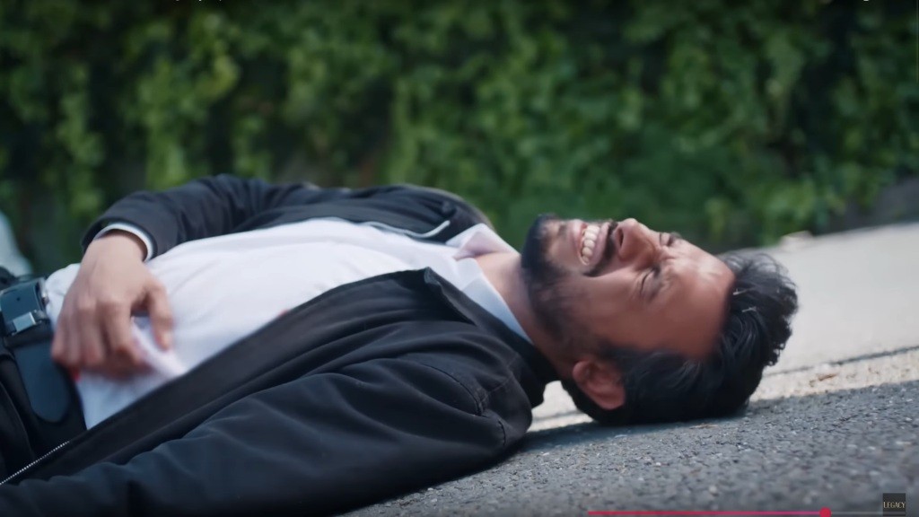 Koray wije się z bólu na ziemi, trzymając się za bok, gdzie został postrzelony.