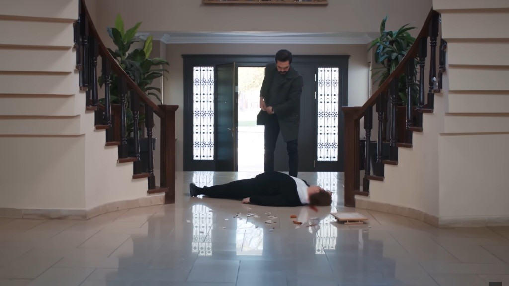 Yaman stoi w hallu nad nieprzytomną Adalet. Sięga ręką do kieszeni po telefon.