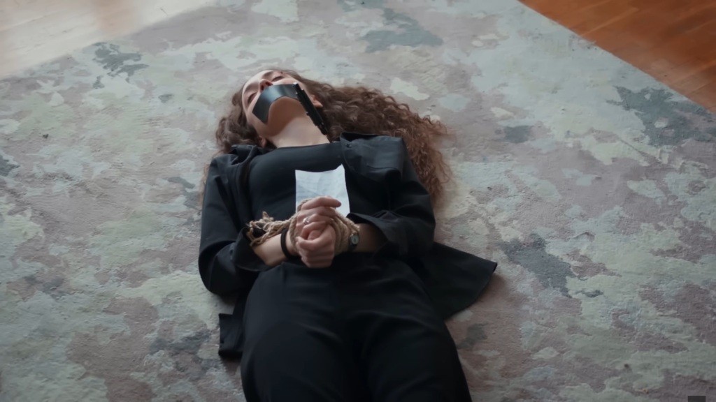 Nana leży na podłodze. Ma związane ręce i zaklejone taśmą usta.