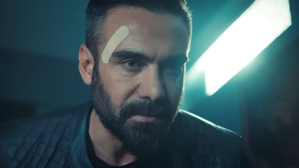 Acar pochyla się i patrzy złowrogo. Na jego skroni znajduje się plaster.