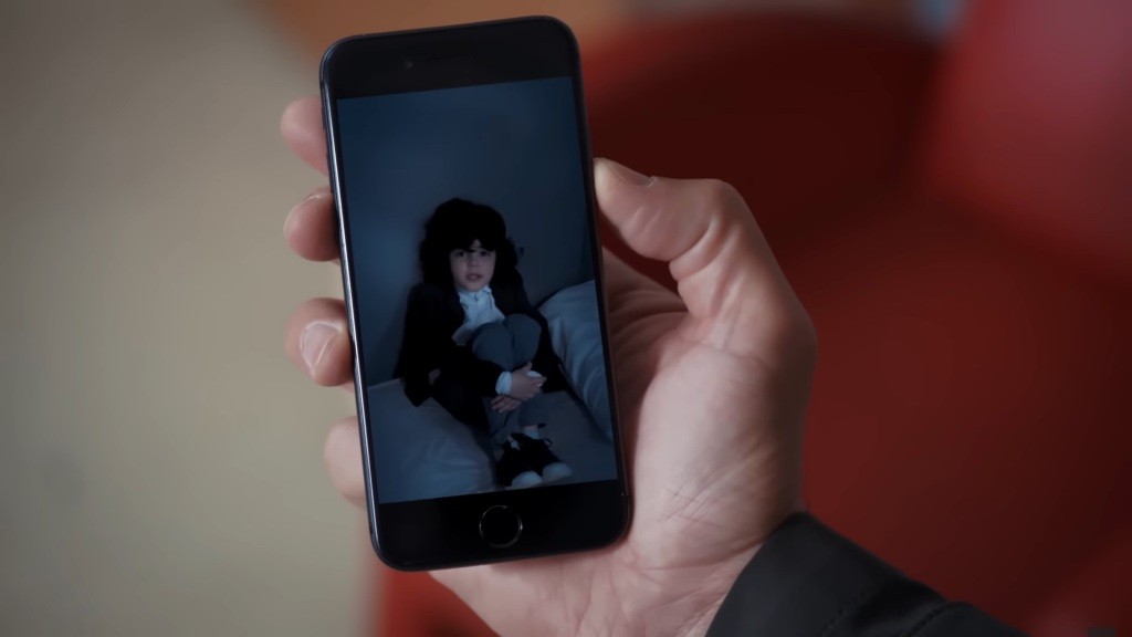 Zbliżenie na telefon, na którym widać skulonego w ciemnym pomieszczeniu Yusufa.