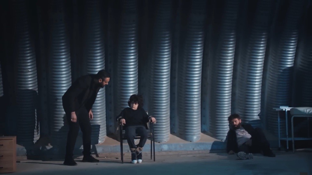 Nowa kryjówka Trucizny. Psychopata pochyla się nad przywiązanym do krzesła Yusufem. Po prawej stronie leży Tunca.