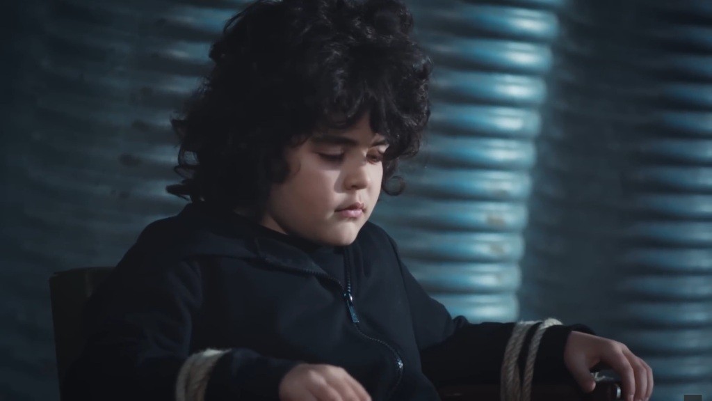 Zbliżenie na nieprzytomnego Yusufa. Jego ręce przywiązane są do krzesła.