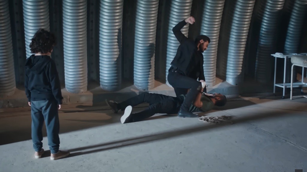 Yaman okłada pięścią powalonego Truciznę. Yusuf obserwuje scenę walki z boku.