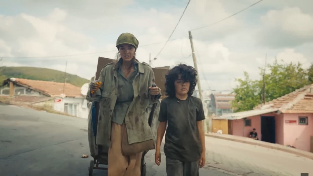 Nana ciągnie wózek z kartonami, a Yusuf idzie przed nią.