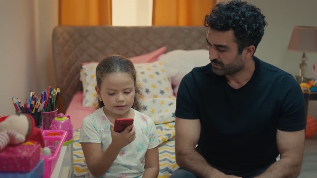 Doga trzyma telefon w rączce. Obok niej siedzi Ferit.