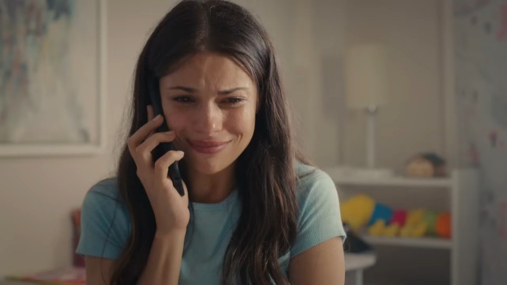 Ayse rozmawia przez telefon. Uśmiecha się, powstrzymując cisnące się do oczu łzy.