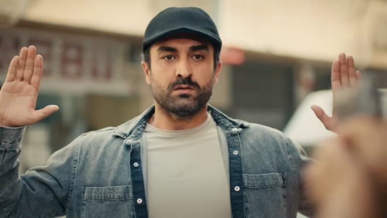 Ferit podnosi ręce do góry, widząc wycelowany w swoją stronę pistolet.