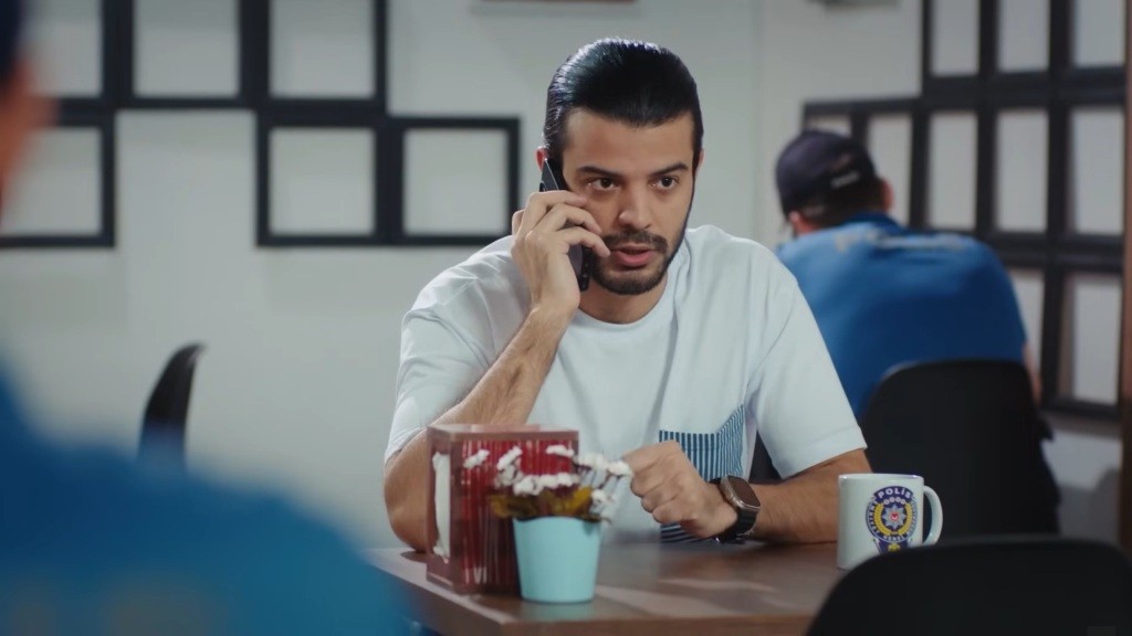 Volkan siedzi przy stoliku w policyjnej stołówce i rozmawia przez telefon.