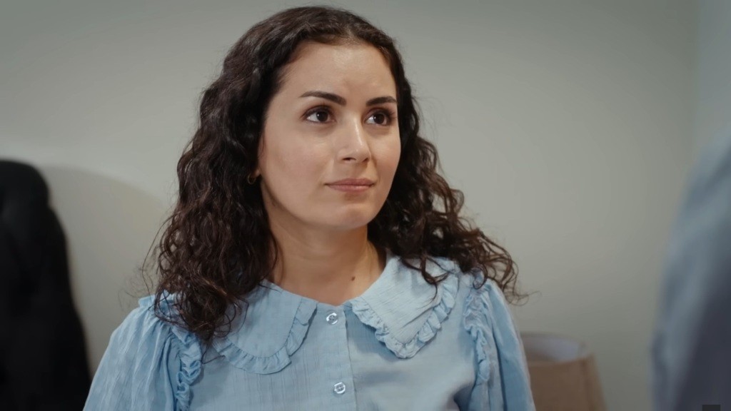 Aynur uśmiecha się subtelnie.