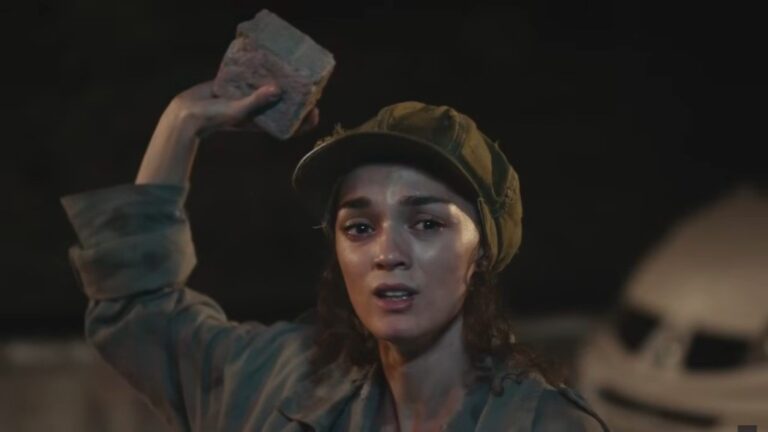 Nana unosi rękę, w której trzyma kawałek cegły.