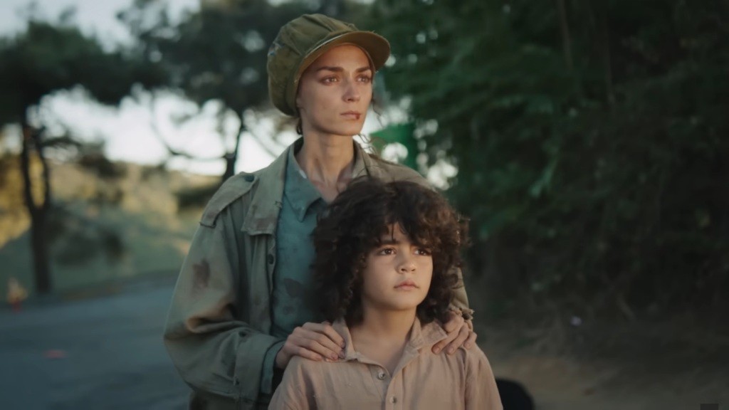 Nana stoi za Yusufem, trzymając ręce na jego barkach.