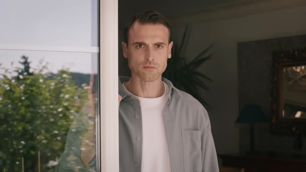 Alper stoi przy drzwiach tarasowych. Jego twarz wyraża napięcie.