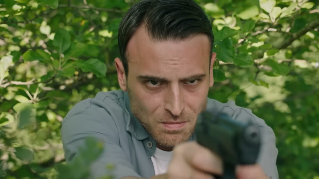 Alper trzyma w ręku pistolet. Na jego twarzy maluje się napięcie.