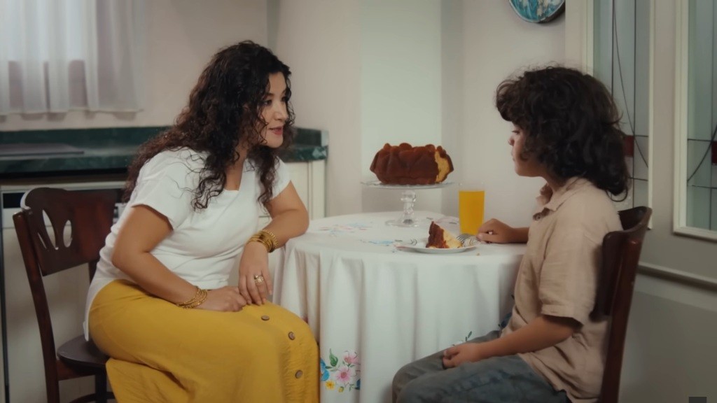 Cansel i Yusuf siedzą przy stoliku. Przed chłopcem leży talerzyk z ciastem oraz szklanka z sokiem.