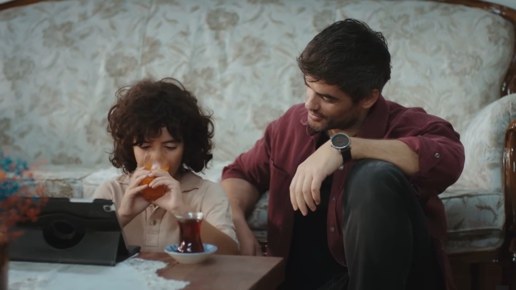 Yusuf pije sok i ogląda kreskówki na tablecie. Poyraz siedzi obok niego.