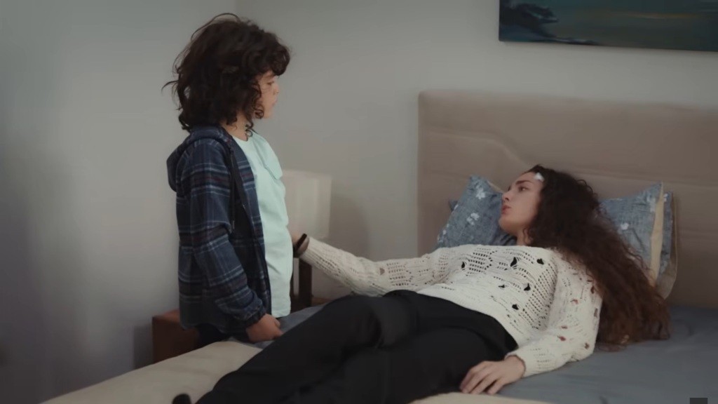 Yusuf stoi przy łóżku Nany. Ona dotyka jego ramienia.