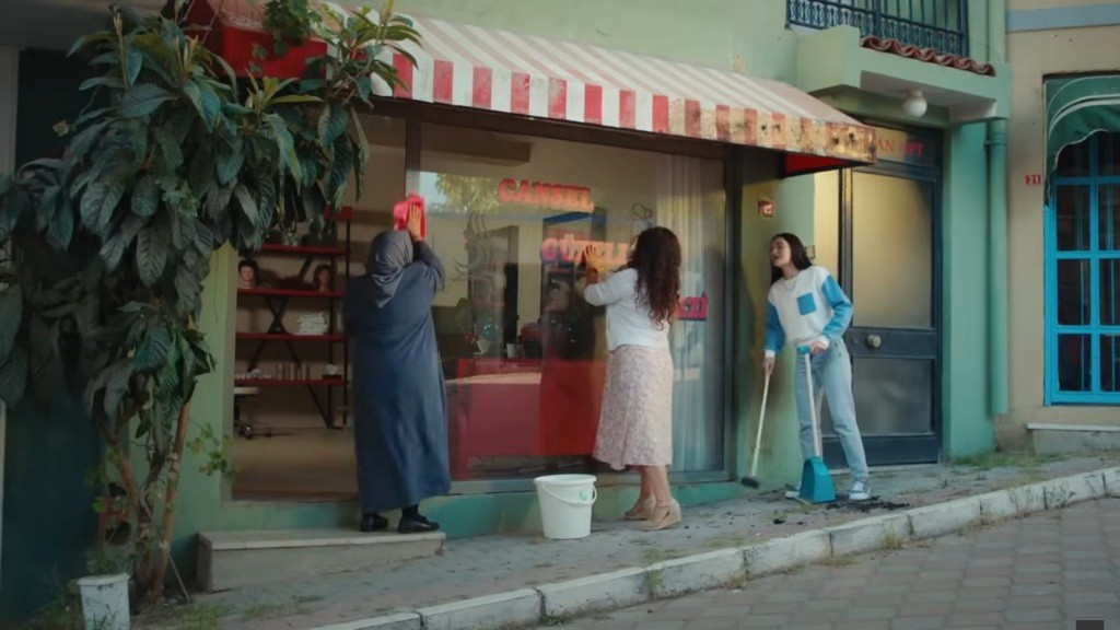 Cennet, Cansel i Nazli myją szybę w zakładzie fryzjerskim.