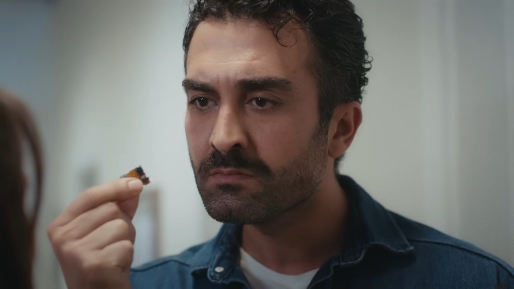 Ferit trzyma urządzenie podsłuchowe między kciukiem a palcem wskazującym.