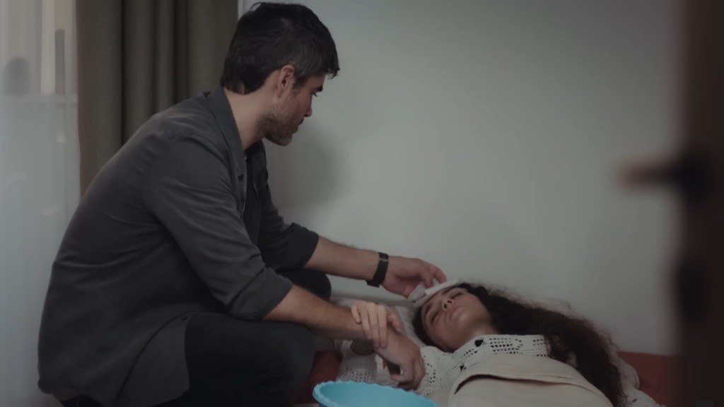 Poyraz przykłada kompres od czoła Nany, a ona chwyta go za rękę.