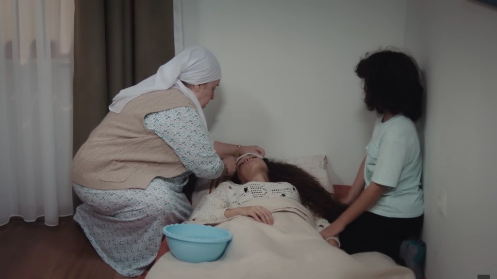 Cennet zmienia kompres na czole Nany. Obok siedzi Yusuf.