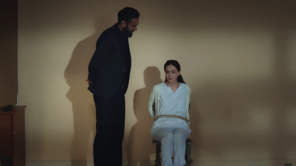 Trucizna stoi obok przywiązanej do krzesła Nazli.