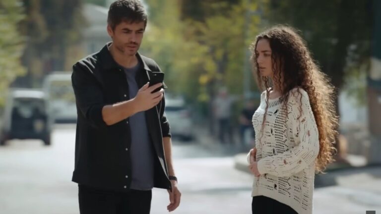 Poyraz trzyma wyciągnięty przed siebie telefon. Obok stoi Nana.