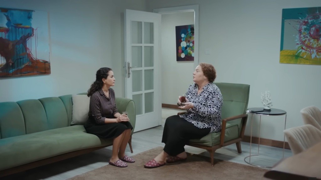 Aynur i Adalet rozmawiają, siedząc naprzeciwko siebie.