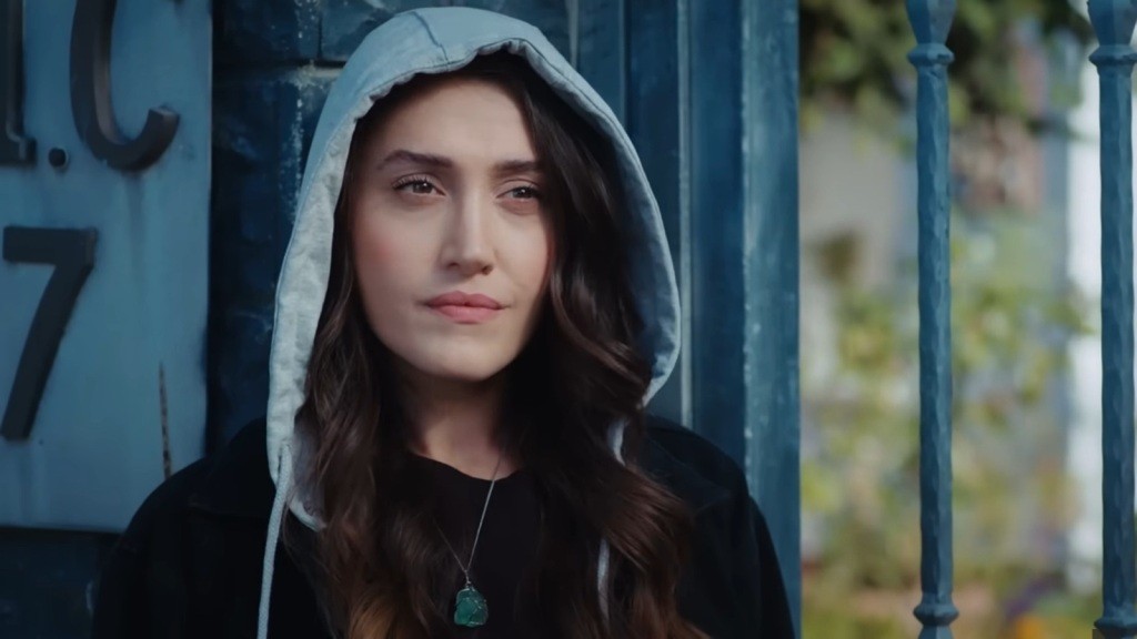 Derya, siostra bliźniaczka prokurator Leyli. Stoi przed bramą, z naciągniętym na głowę kapturem.