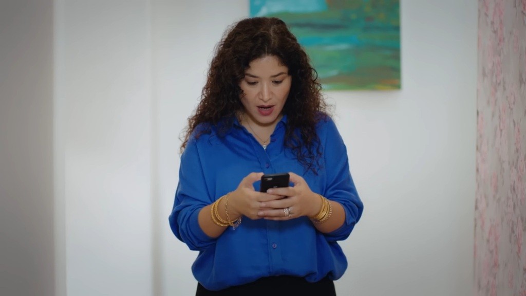 Cansel wpatruje się w ekran telefonu, a na jej twarzy maluje się mieszanka zaskoczenia i zachwytu.