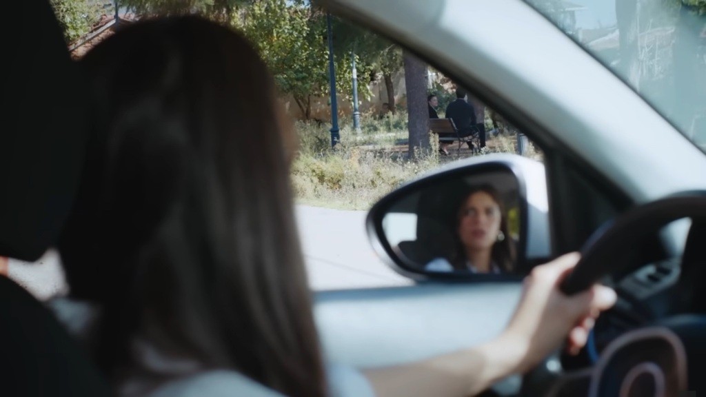 Kobieta spogląda przez boczne okno samochodu, a w lusterku bocznym odbija się jej twarz.