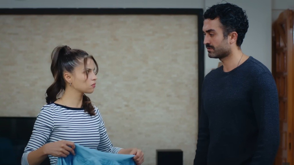 Ayse składa ubrania. Obok niej stoi Ferit.