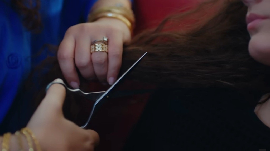 Cansel trzyma w jednej ręce pasmo włosów Nany, a w drugiej nożyczki.