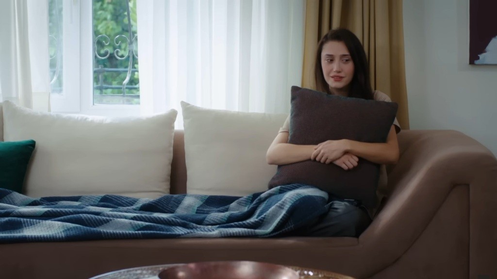 Derya siedzi na kanapie, tuląc do siebie poduszkę.