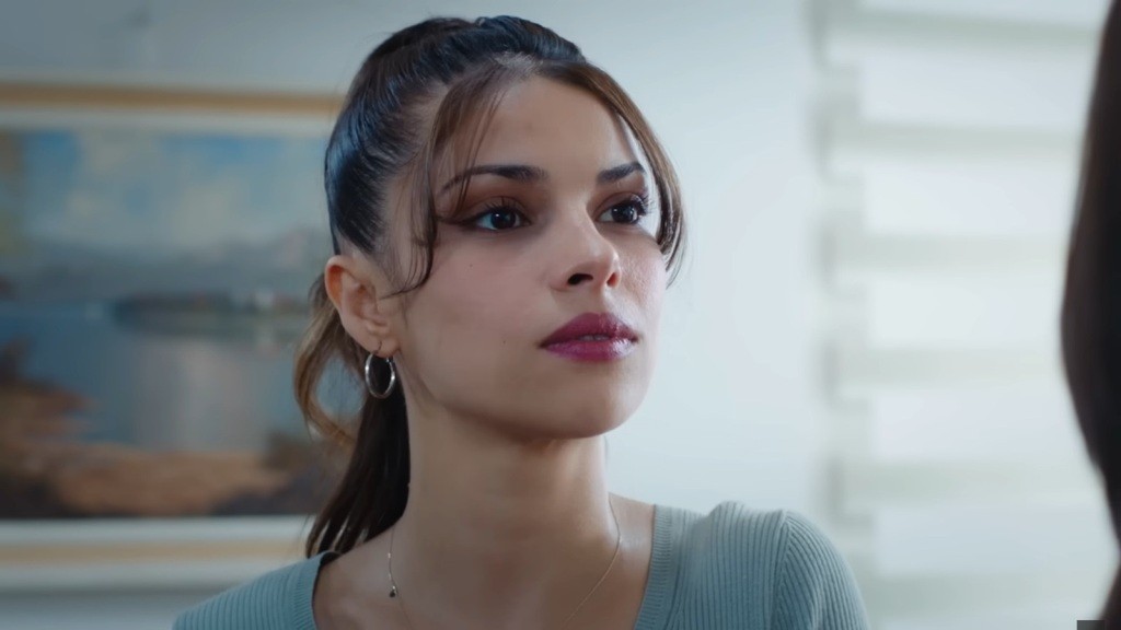 Ayse unosi głowę, patrząc z determinacją.