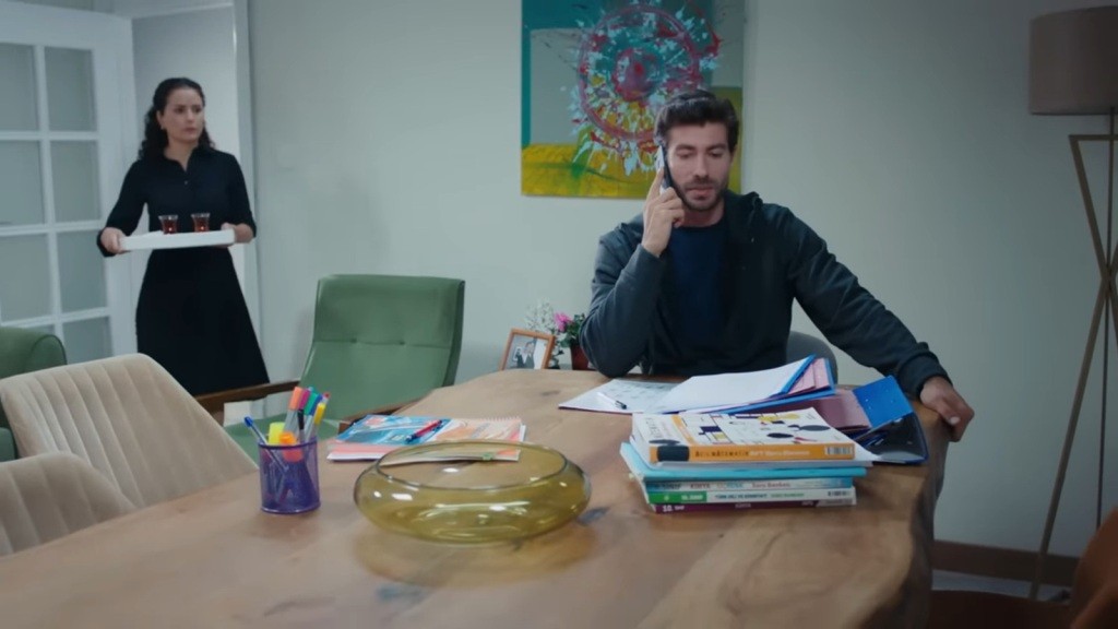 Sinan rozmawia przez telefon. Do pokoju wchodzi Aynur z tacą w rękach.
