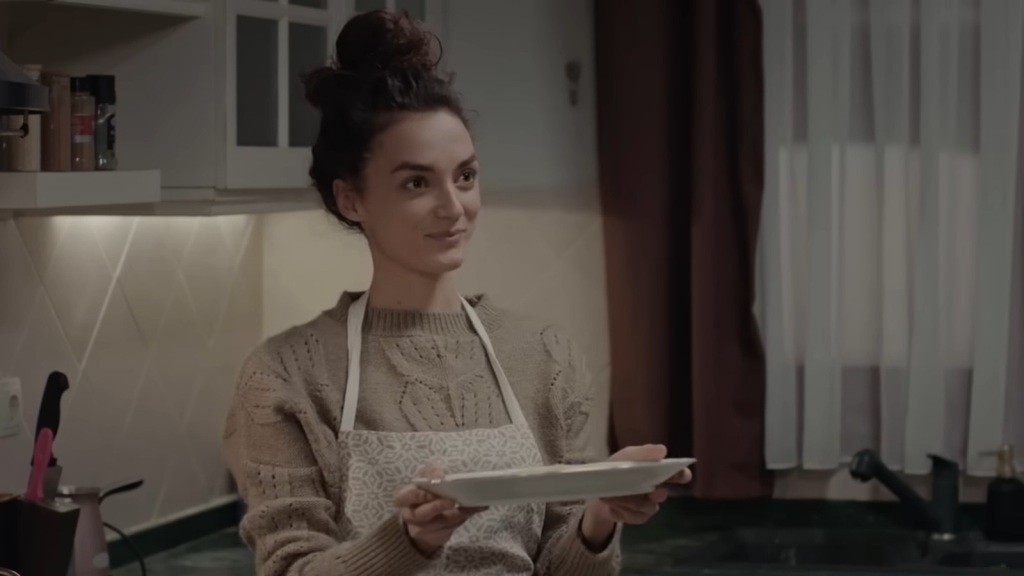 Nana ma na sobie fartuszek kuchenny. Trzyma w rękach talerz uśmiechając się.