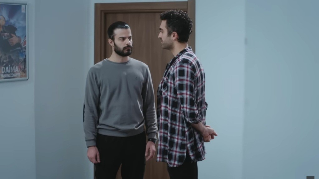 Volkan i Ferit rozmawiają, stojąc na korytarzu obok siebie.