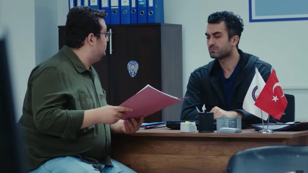 Ibrahim i Ferit rozmawiają, siedząc przy biurku.