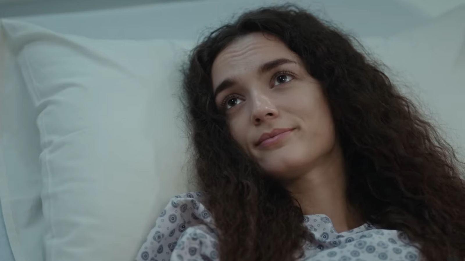 Nana leży na łóżku szpitalnym i uśmiecha się delikatnie.