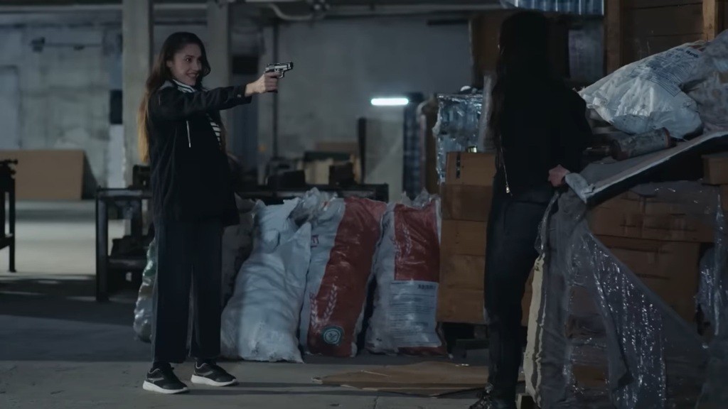 Scena w magazynie. Derya śmieje się, celując do Ayse z pistoletu.