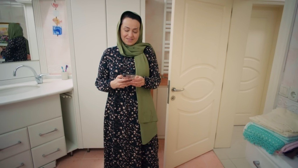 Cavidan znajduje się w łazience. Trzyma w rękach telefon, uśmiechając się przebiegle.