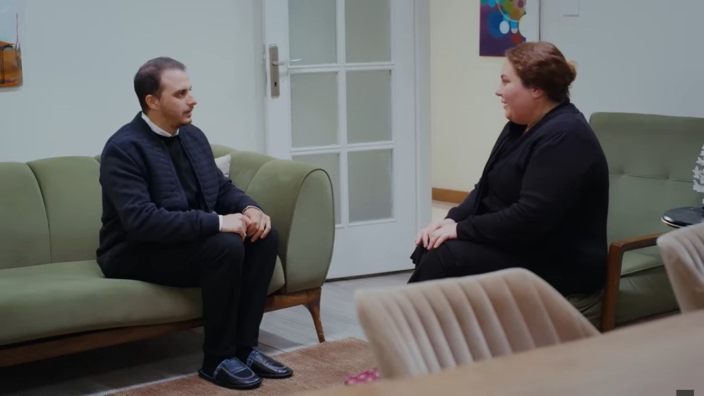 Adalet rozmawia ze swoim sąsiadem w salonie.