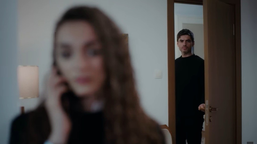 Poyraz stoi przy uchylonych drzwiach pokoju, skąd podsłuchuje rozmowę telefoniczną Nany.