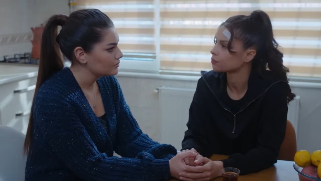 Nese i Ayse siedzą przy stole w kuchni, ujmując swoje dłonie i patrząc sobie w oczy.