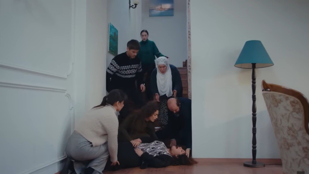 Cansel leży na podłodze przed schodami. Domownicy zebrali się wokół niej.