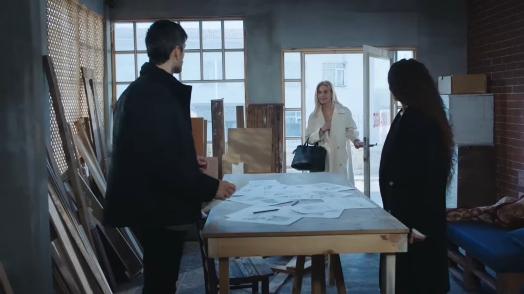 W drzwiach warsztatu staje kobieta o blond włosach.