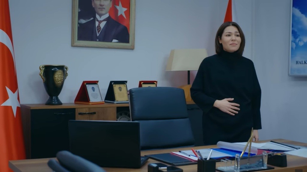 Kara trzyma się za brzuch, stojąc w swoim gabinecie. Na jej twarzy maluje się rozmarzenie.