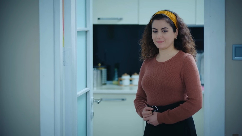 Aynur stoi przy samym wejściu do kuchni. Na jej twarzy maluje się delikatny uśmiech.
